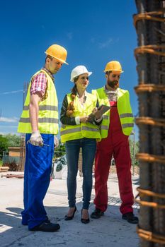 Female manager or architect between two workers supervising the work in progress on the construction site of a building with reinforcing steel structure