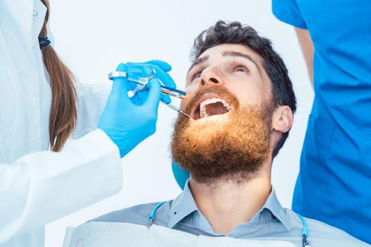 Low-angle close-up view of a man with the mouth open during a medical procedure in the dental office of an experienced female dentist