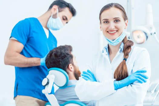Portrait of a happy and confident female dentist wearing sterile white coat and surgical gloves, while looking at camera in the dental office of a modern clinic with reliable specialists