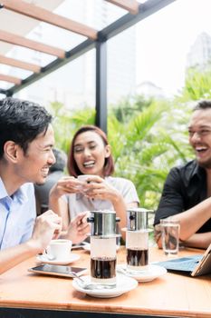 Delicious Vietnamese coffee served on the table of three young cheerful Asian friends outdoors in a modern cafeteria