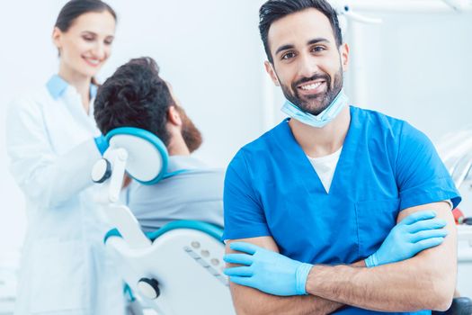 Portrait of a confident dental surgeon wearing blue protective uniform and surgical mask while looking at camera in a modern dental office with reliable specialists