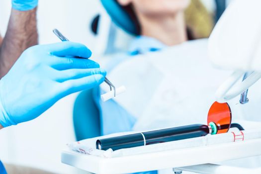 Close-up of the hand of a dentist wearing sterile surgery gloves, while preparing a dental LED curing light machine for treating a patient in a modern clinic