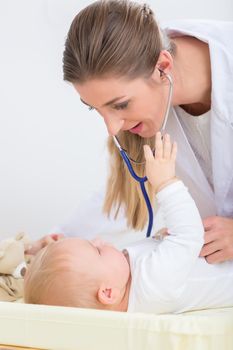 Dedicated female pediatrician using the stethoscope during the routine medical check-up of a cute and healthy baby girl in a modern healthcare center