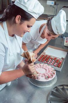 Confectioner women putting cream on cake finishing the pastry