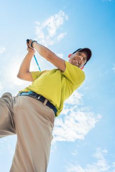 Low-angle view of a professional player wearing golf outfits while holding the club ready for the strike during individual game outdoors against cloudy sky