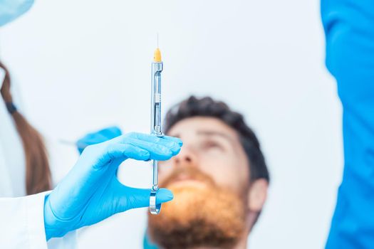 Close-up of the hand of a female dentist wearing sterile surgical glove while holding a dental anesthetic syringe before treating a patient