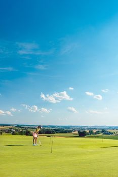 Full length of a determined young woman practicing golf moves and strikes on the grass of a training area for putting green, in an idyllic sunny rural place