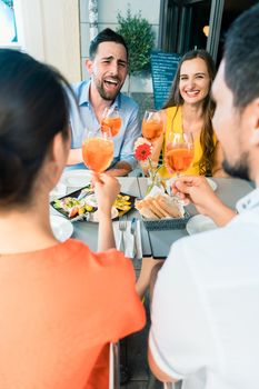 Two happy young couples with a trendy lifestyle toasting while sitting together at restaurant for a delicious lunch outdoors in summer