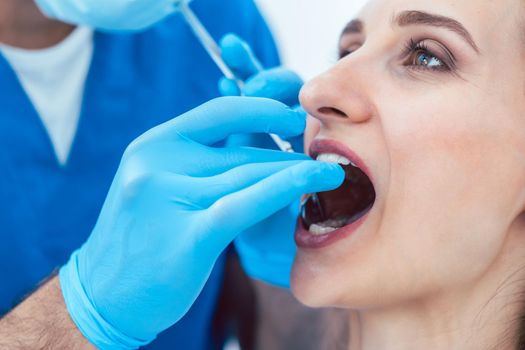 Close-up of the hands of a dentist wearing surgical gloves and using sterile medical equipment, while cleaning the teeth of a young woman in a modern dental clinic