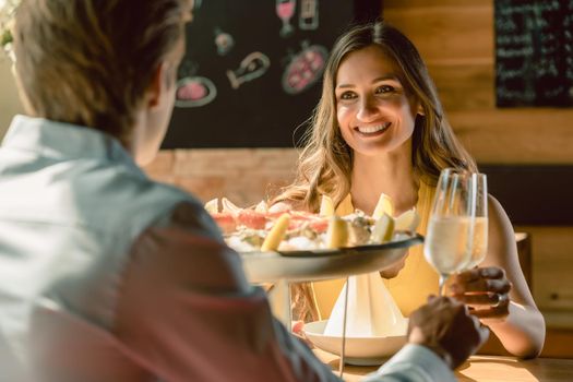 Happy young couple in love toasting with champagne during romantic dinner with seafood as oysters and crabs at the restaurant