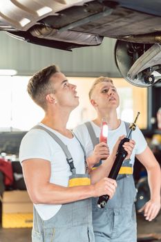 Side view of a skilled auto mechanic replacing the shock absorbers of a lifted car, while working together with his colleague in a modern automobile repair shop