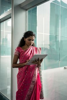 Portrait of young Indian woman using a tablet PC outdoors against the glass wall of a modern business building