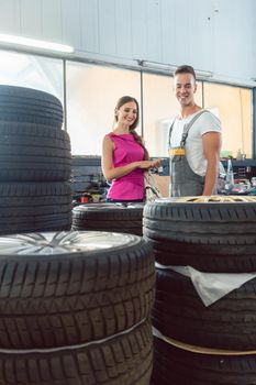Handsome auto mechanic helping a female customer to choose from various high-quality tires in a contemporary automobile repair shop