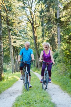 Full length of a happy and active senior couple wearing cool fitness outfits while riding bicycles outdoors in the park