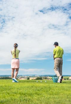 Full length of a young woman smiling while practicing the correct move for striking during golf class with a skilled professional player outdoors