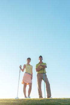 Low-angle view of the silhouette of a man pointing to the horizon, while standing next to his female partner on a professional golf course against sunshine and clear blue sky