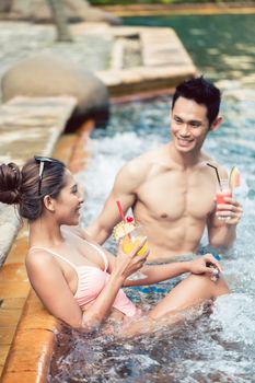 Handsome young man flirting with an attractive woman while drinking delicious cocktails in a trendy swimming pool during summer vacations