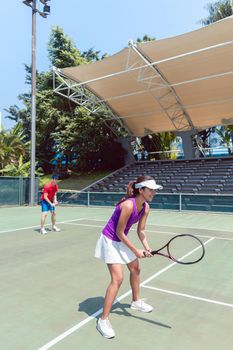 Full length of a confident female tennis player smiling while waiting to hit the ball during doubles match on a professional modern court