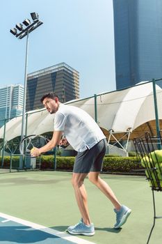 Low-angle view of a young handsome man ready to serve while playing tennis outdoors in a modern district of the city