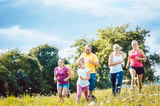 Family running on a meadow with flowers for sport