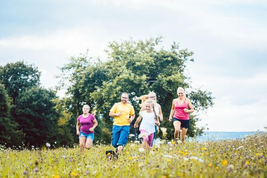 Family running on a meadow with flowers for sport