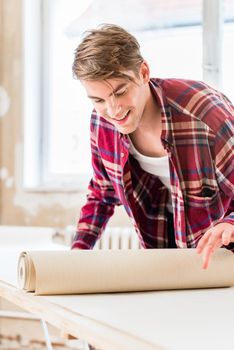 Handsome young man applying paste with a synthetic brush to the surface of a wallpaper sheet during home remodeling