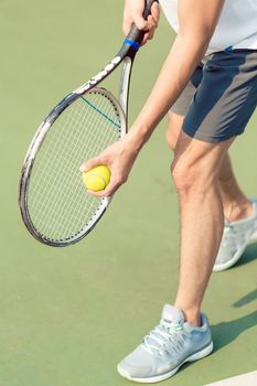 Low section of a professional player wearing gray sport shoes while holding the ball and the tennis racket during match on green surface