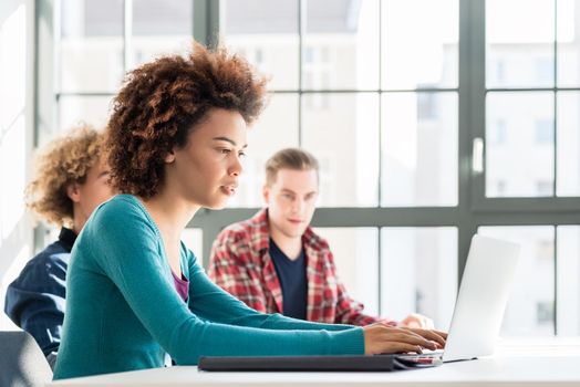 Side view of a happy student smiling while using a laptop for online information or virtual communication through social media during class at the university