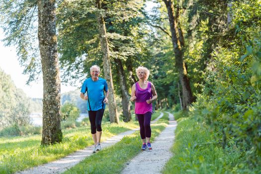 Full length front view of two active seniors with a healthy lifestyle smiling while jogging together outdoors in the park