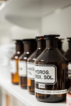 Close-up of the labeled glass container of a chemical pharmaceutical substance on a shelf, next to various supplies in the storage of a modern drugstore