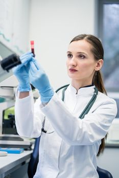 Doctor in medical laboratory looking at blood test she is holding in her hand