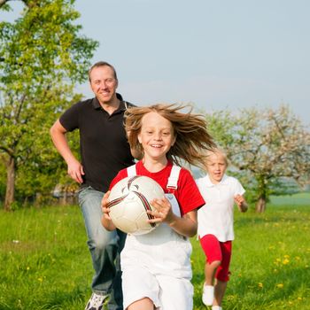 Happy family playing football, one child has grabbed the ball and is being chased by the others