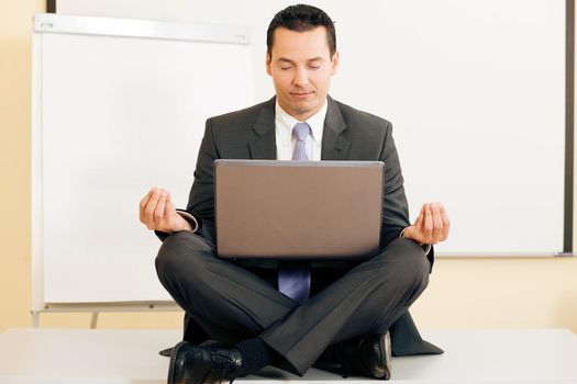 Office worker - a male manager - meditating cross legged upon his table, being very relaxed, a metaphor for work life balance