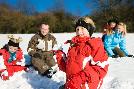 Family with kids having a snowball fight in winter on top of a hill in the snow