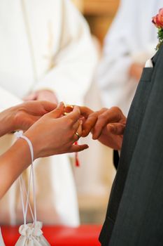 Couple having their wedding ceremony in church in front of a catholic priest, slipping the ring over each other's finger