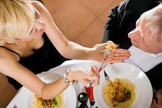 Romantic mature couple having dinner, she feeding him with delicious pasta