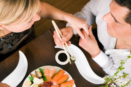 Couple eating sushi for dinner, romantic setting, presumably this is an advanced date; shallow focus on eyes