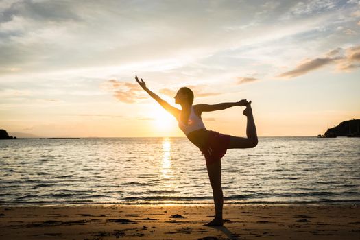 Full length side view of a fit woman practicing on the beach. The standing bow pulling pose for muscular strength and flexibility during summer vacation in Indonesia