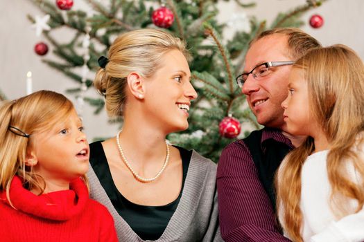 Family sitting on Christmas day in front of the Christmas tree, smiling