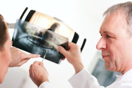 Dentist explaining the details of a x-ray picture to his patient, focus on eyes of doctor