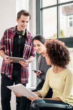 Three young employees using modern devices with wireless connection to internet during break in the office