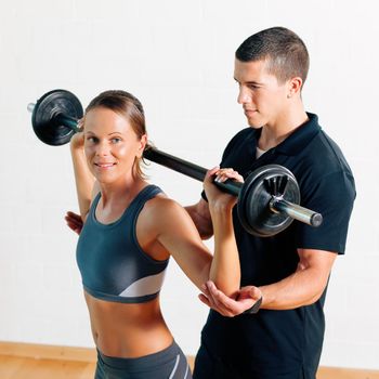 Woman with her personal fitness trainer in the gym exercising power gymnastics with a barbell