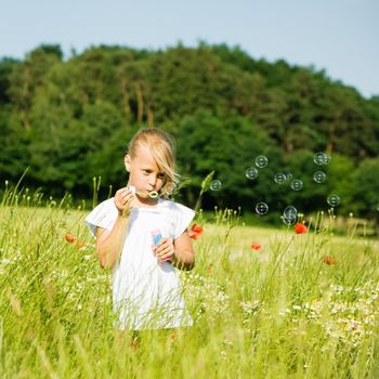 Little girl in a field making soap bubbles and having fun with it