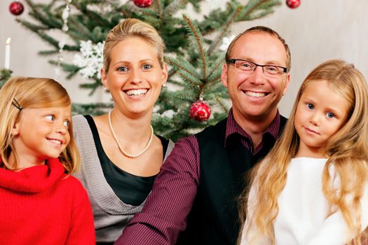 Family sitting on Christmas day in front of the Christmas tree, smiling