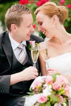 Newlywed couple - bride and groom - clinking glasses with champagne after their wedding