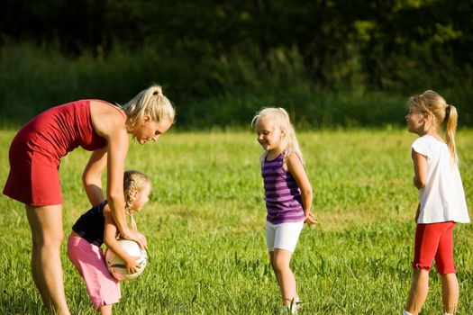 Mother with three daughters playing football (well, soccer for North America) on a green, sunlit meadow