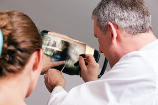 Dentist explaining the details of a x-ray picture to his patient, focus on eyes of doctor