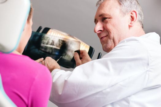 Dentist explaining the details of a x-ray picture to his patient, focus on eyes of doctor