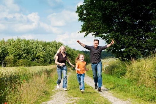 Happy family (mother, father and kid) having a walk in the nature playing tag