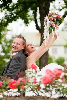 Visibly happy newlywed couple sitting in a park with a lot of roses in foreground